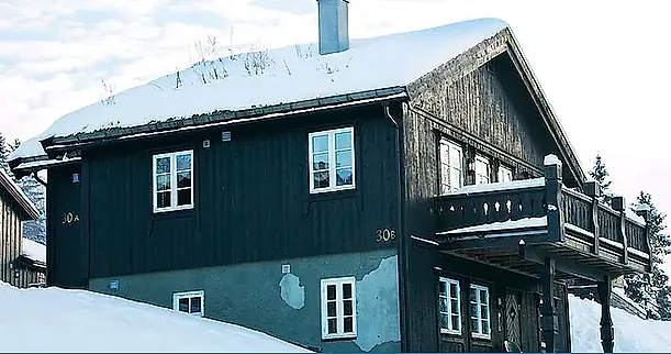 Tømmerhus i to etasjer med snødekt tak og veranda.